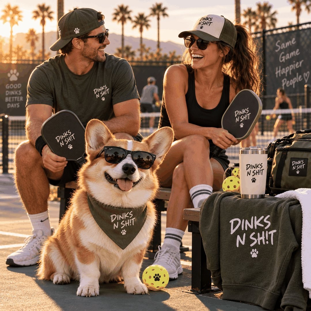 A couple and their sunglasses-wearing corgi courtside at sunset with Dinks N Sh!t tees, hats, paddles and a tumbler